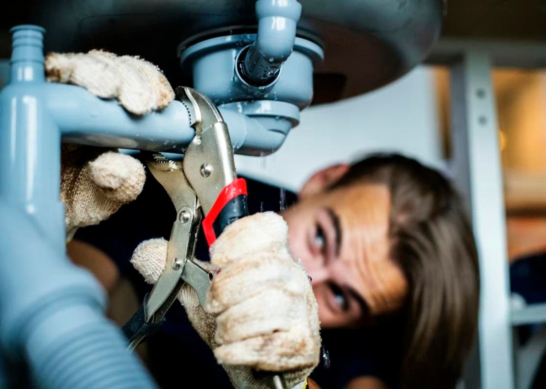 A plumber fixing a pipe leak under sink